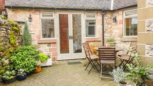 Une maison en pierre avec un toit en tuiles, une porte en verre et une terrasse avec une table et des chaises.
