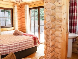Habitación de cabaña de madera con cama, ventana, baño con lavamanos y vistas al exterior.