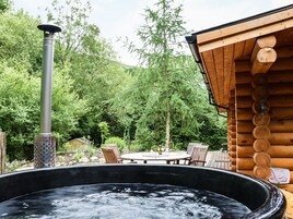 Un jacuzzi rodeado por una terraza de madera, con una chimenea y un comedor al fondo.