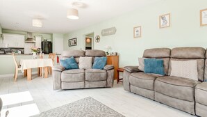 A spacious living room with a grey sofa set, a dining area with a white table, and a kitchen in the background. - Kingfisher Lodge (Driffield)