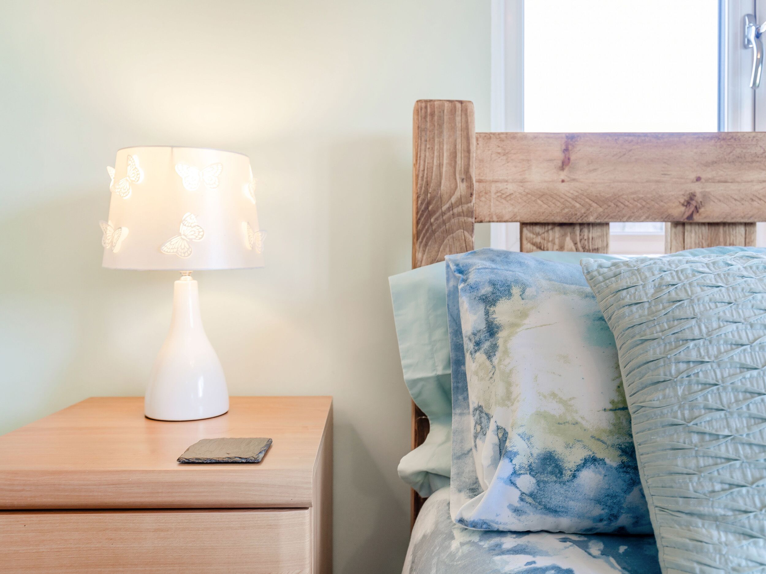 A wooden nightstand with a white lamp and a smartphone.