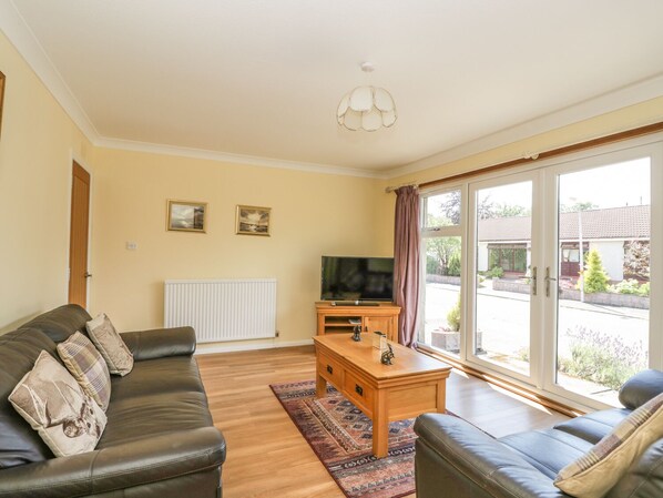 A living room with a sofa, a coffee table, and a television. There are two framed pictures on the wall and a window with curtains. - Isla Cottage (Blairgowrie)