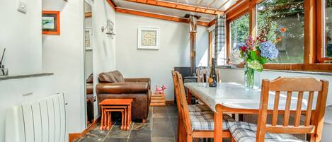 A cozy dining area with a wooden table and chairs, a brown leather sofa, and a small wooden stool.