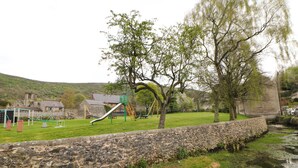 A playground with a slide and swings, a stone wall, and a stream. - Brookside Barn (Hope Valley)