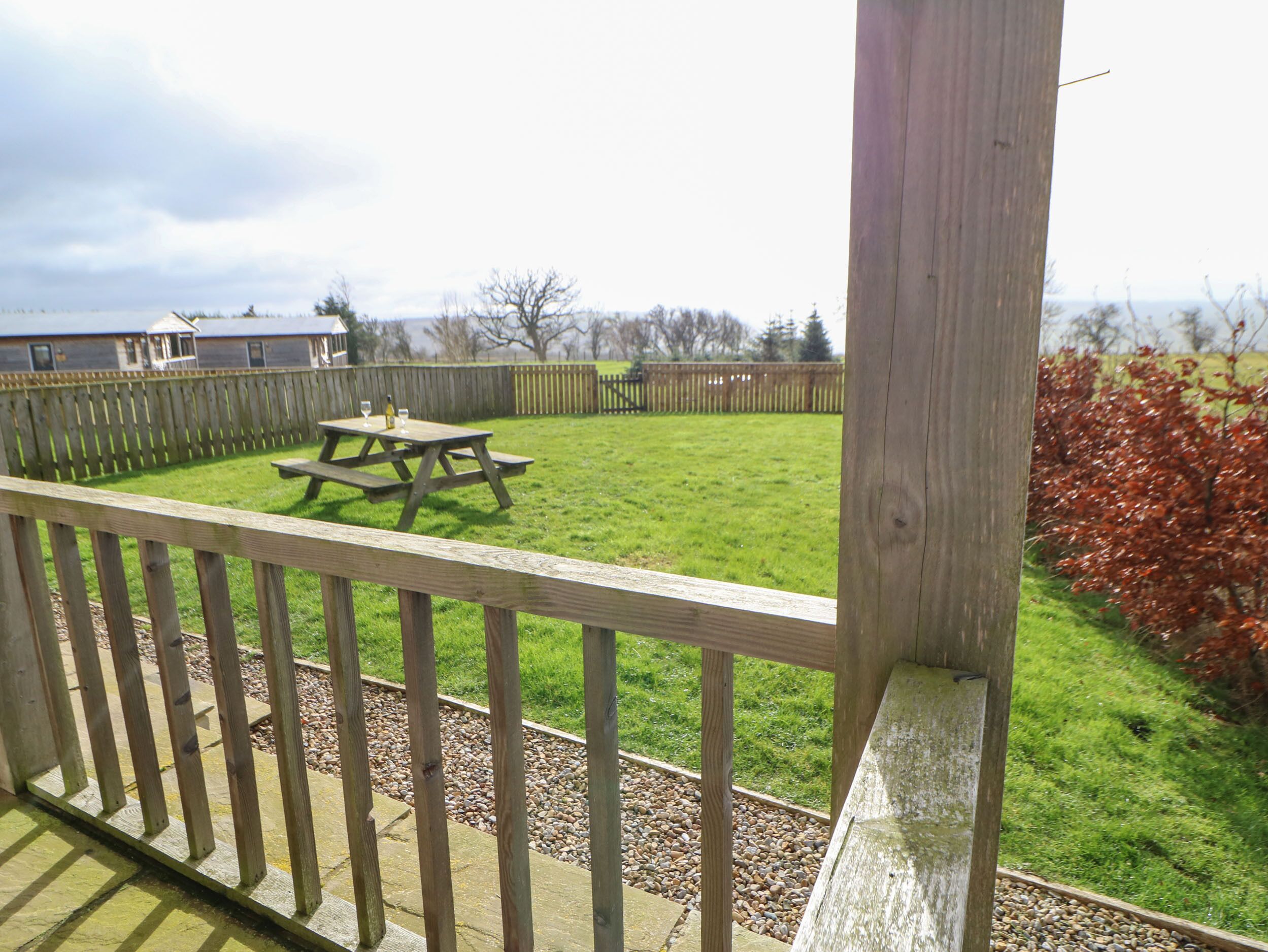A wooden deck with a picnic table and a view of a grassy yard.