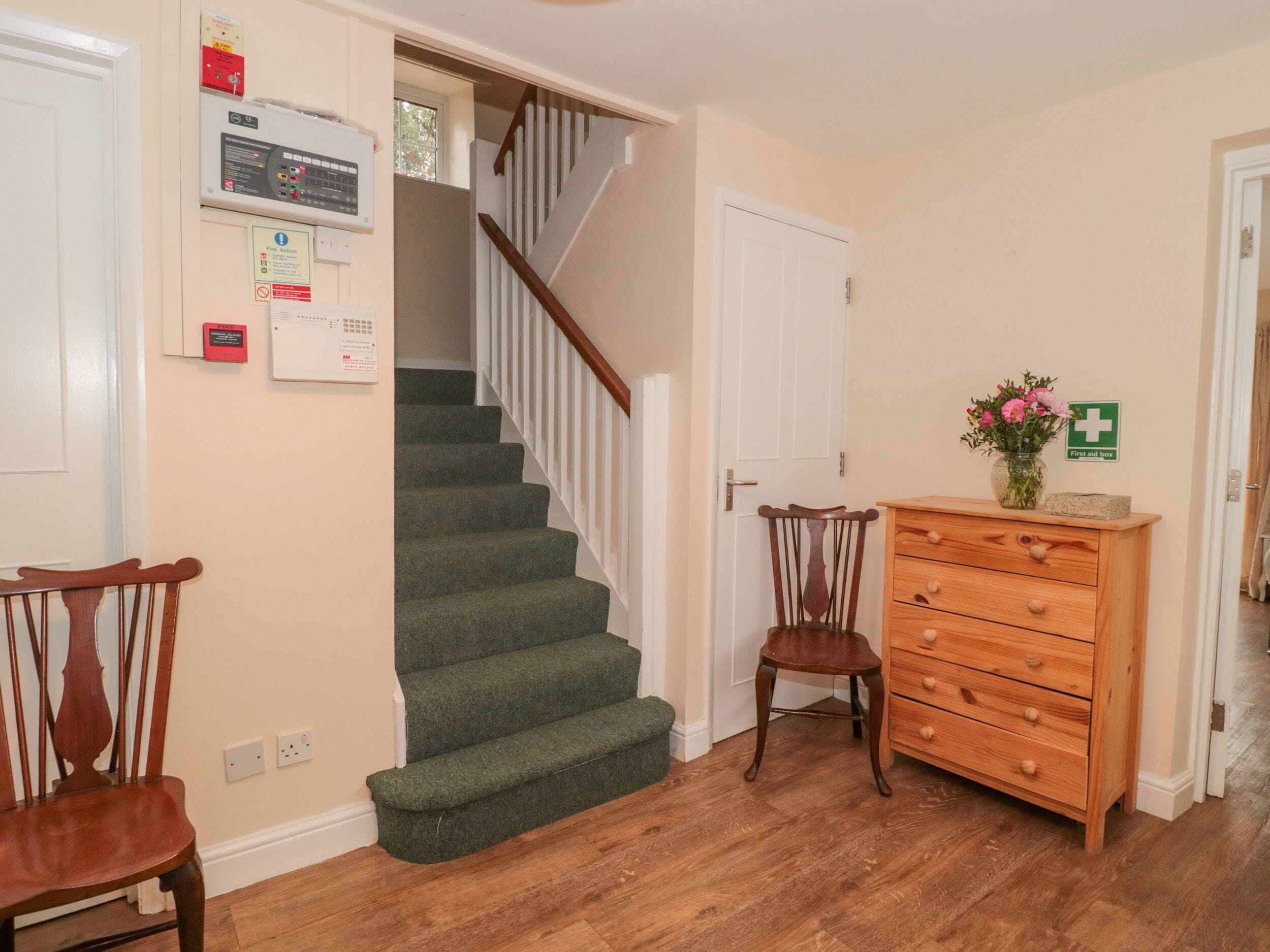 A staircase with carpeted steps, a wooden chair, a wooden dresser, and a first aid box sign on the wall.