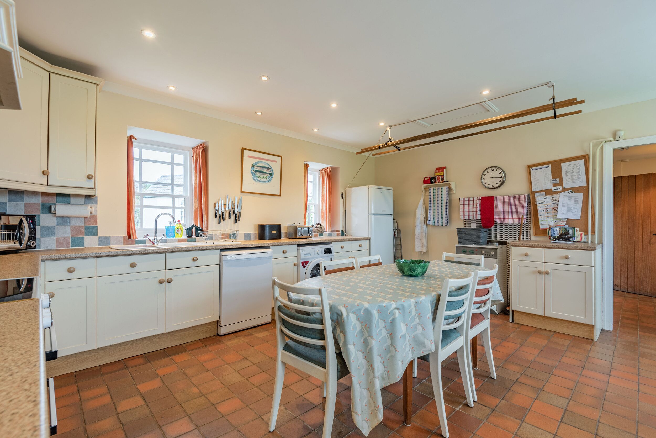 A kitchen with white cabinets, a dining table with chairs, a refrigerator, and a window with curtains.