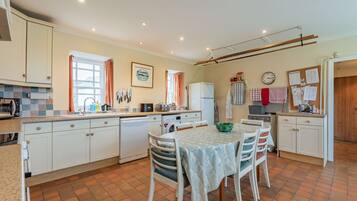 A kitchen with white cabinets, a dining table with chairs, a refrigerator, and a window with curtains.