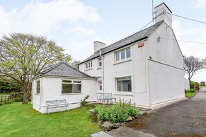 Une maison à deux étages avec un petit garage séparé, un jardin agrémenté d’un banc et une allée pavée.