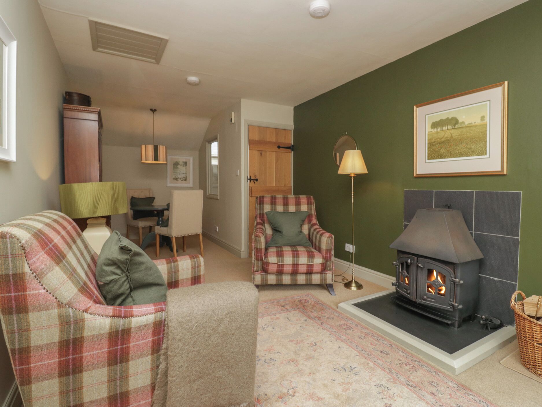 A cozy living room with a fireplace, plaid furniture, and a dining area with a lamp.