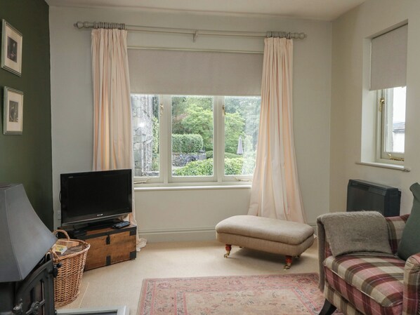 A room with a television, a fireplace, a window with curtains, a sofa, and a rug.