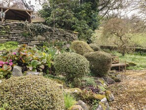 A garden with stone walls, various plants, and a wooden bench.