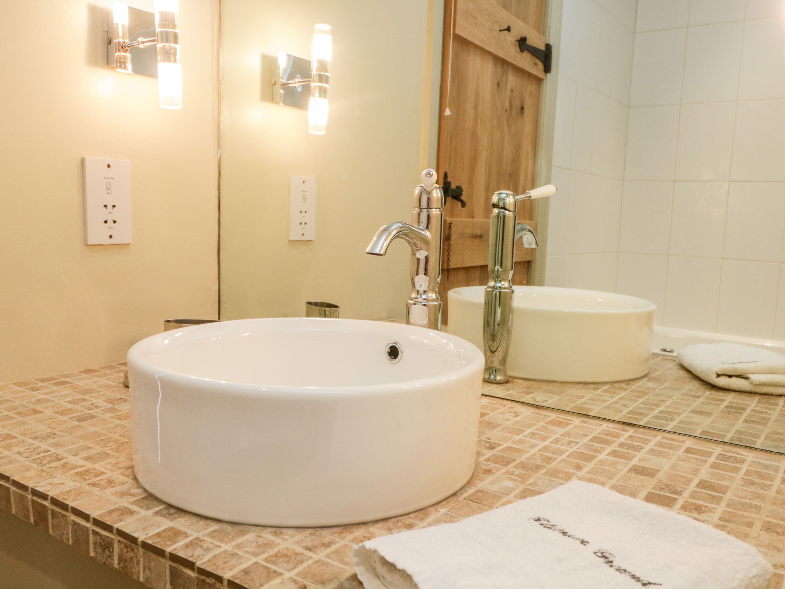 A bathroom with a round white sink, a mirror, and a wooden door.