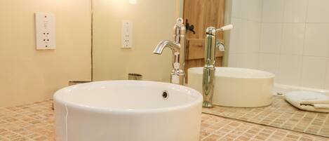 A bathroom with a round white sink, a mirror, and a wooden door.