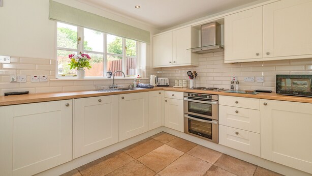 A modern kitchen with white cabinets, a wooden countertop, a built-in oven, and a window with a flower vase. - 4 Aldelyme Court (Crewe)