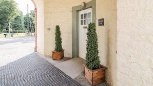 A building entrance with a white door, two potted plants, and a sign reading "The Mews Flat". - The Mews Flat (Dumfries)