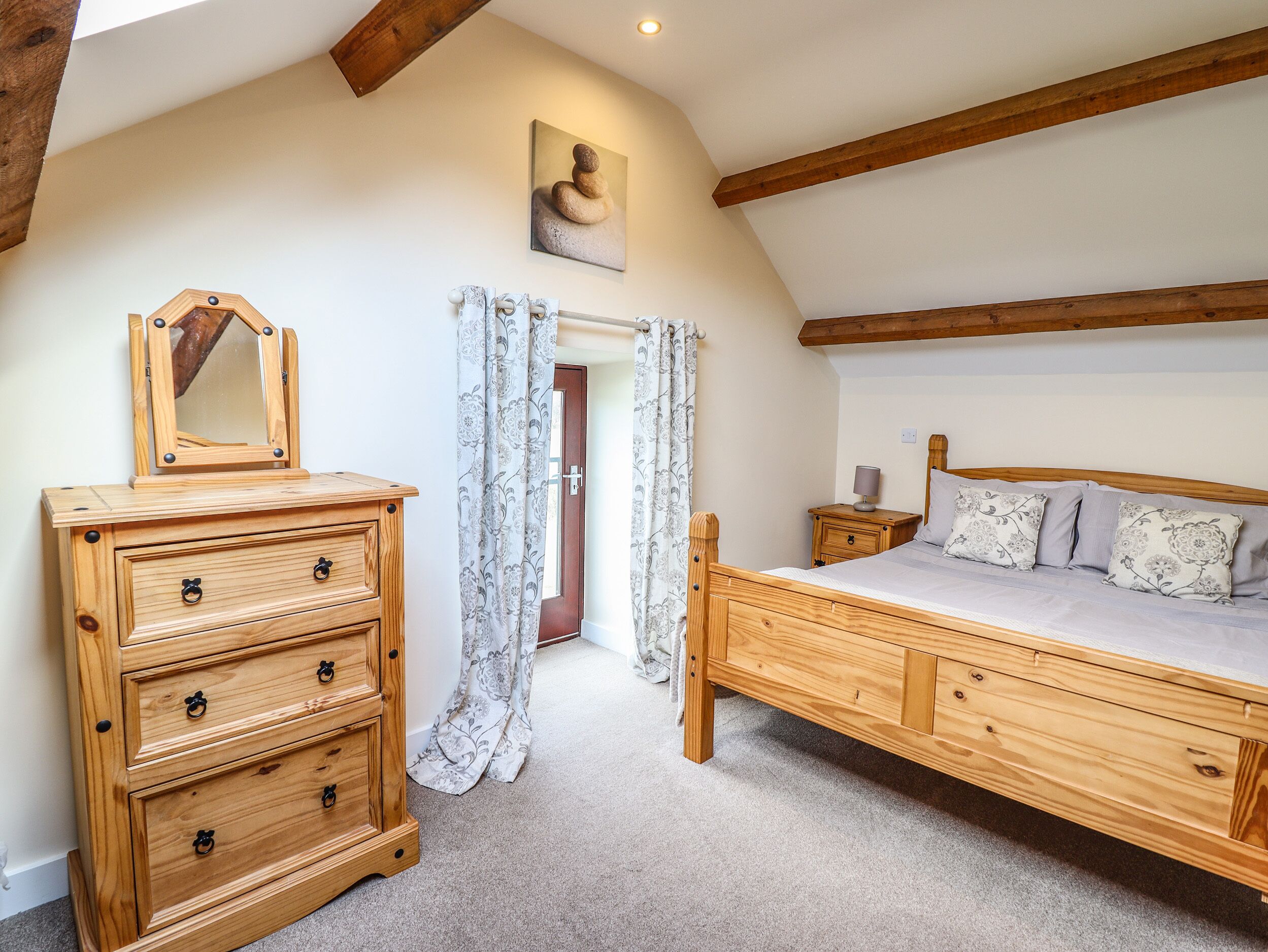 A bedroom with a wooden bed, a dresser, a mirror, and a painting on the wall.