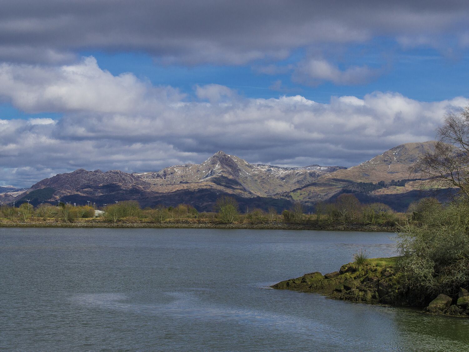 A lake with mountains in the background and a cloudy sky.