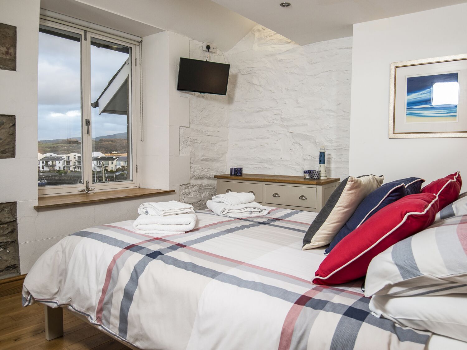 A bedroom with a bed, a bedside table, a TV, a window, and a view of buildings outside.