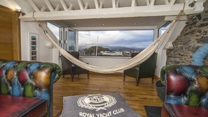 Een kamer met een hangmat, leren fauteuils en uitzicht op een stad en bergen.