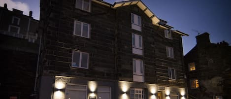 Un edificio de varios pisos de piedra con techo plano, múltiples ventanas y una entrada principal.