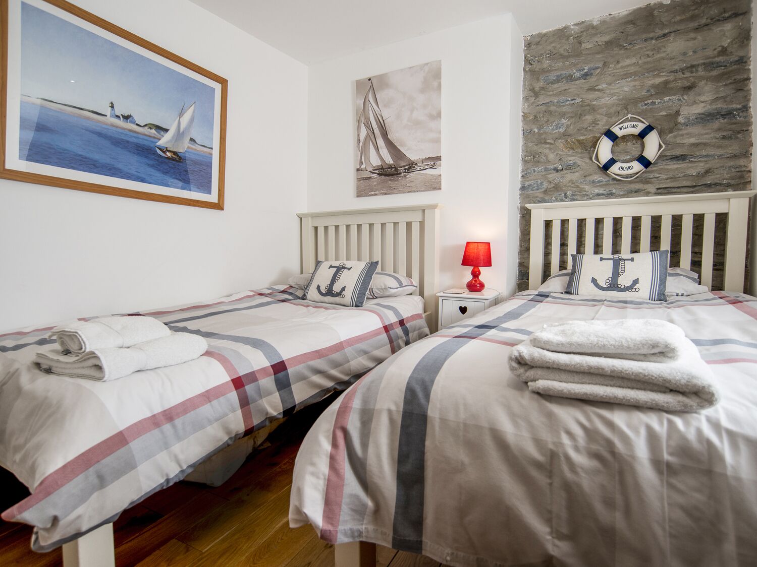 A bedroom with two beds, striped bedding, a red lamp, nautical-themed decor, and a life preserver on the wall.