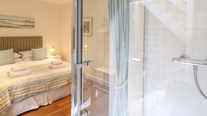 Une chambre d’hôtel moderne dotée d’une douche en verre, d’un lit avec une couvre-lit à rayures et d’une tête de lit avec des lattes verticales.