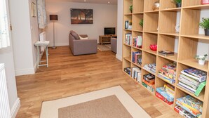 A modern living room with a grey sofa, wooden bookshelf, and a painting on the wall. - The Dower House Cottage (Bedale)