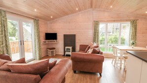 Ein geräumiges Wohnzimmer mit Holzwänden und -böden, einem Kamin, einem Fernseher und einem Essbereich mit Tisch und Stühlen.