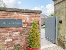 A brick wall with a sign reading "GREY ROOFS" and a potted evergreen shrub.