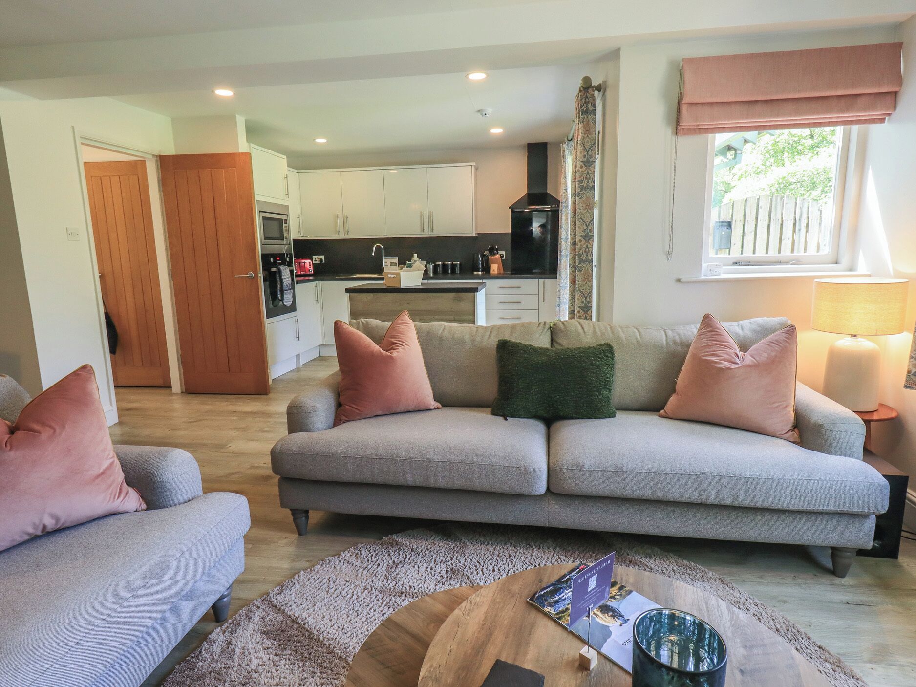 A living room with a grey sofa, a wooden coffee table, and a kitchen in the background.