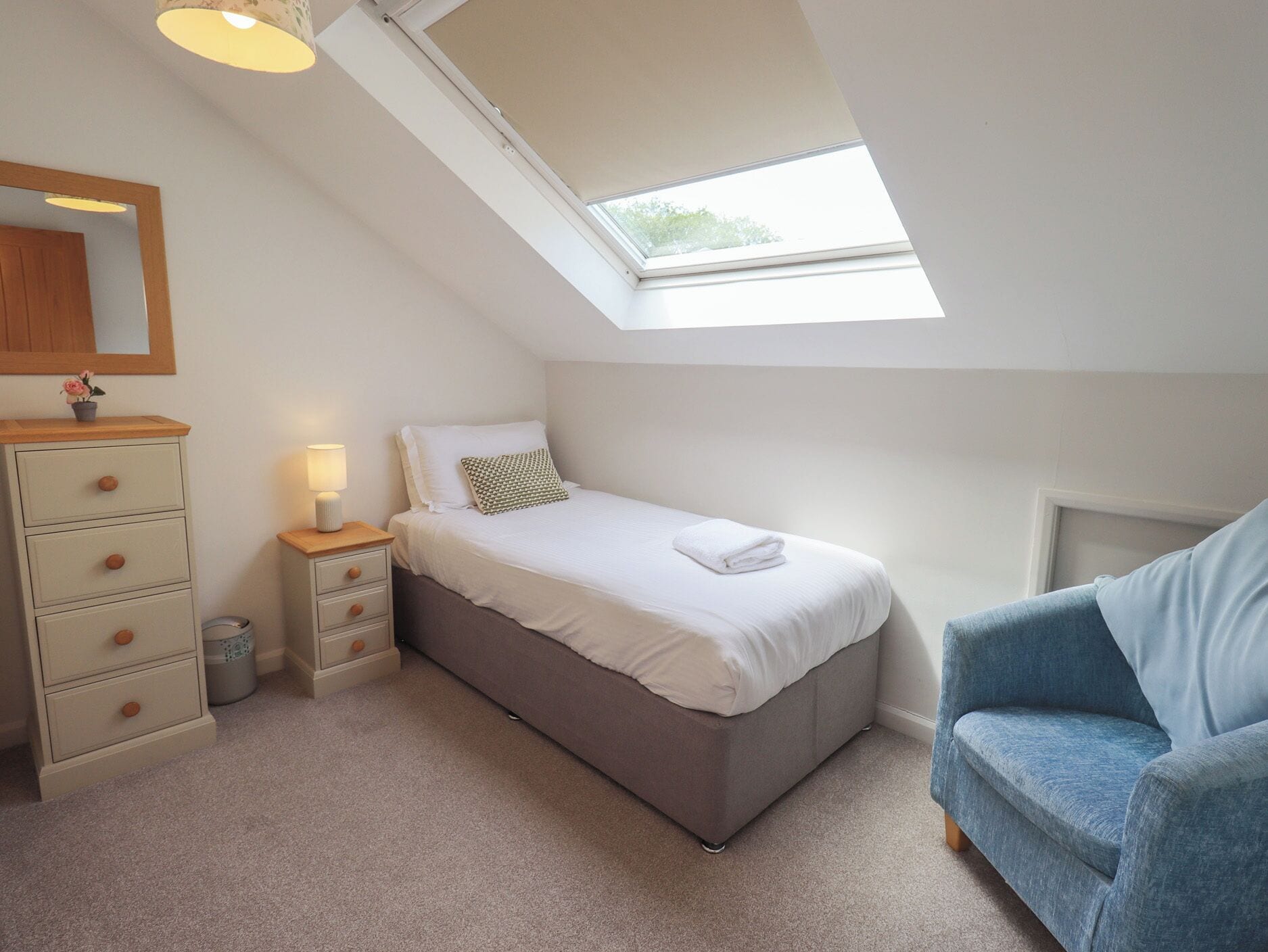 A bedroom with a skylight, a bed, a nightstand, a dresser, and a chair.