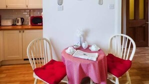 A dining area with two white chairs, a table with a red and white checkered tablecloth, and a wall clock.