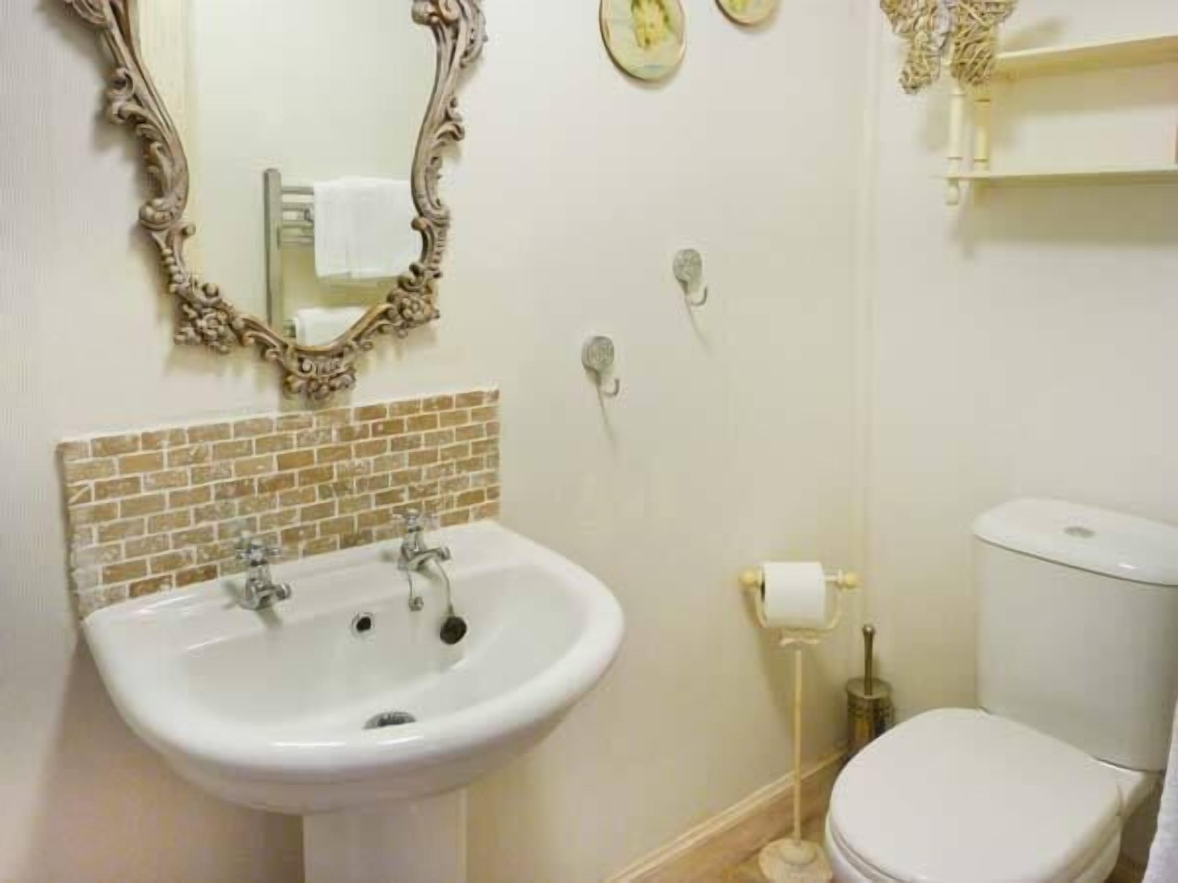 Un baño con lavamanos blanco, inodoro y espejo decorativo.