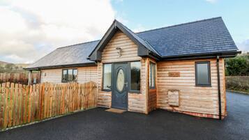 A log cabin with a dark roof, a front door with a glass panel, and a sign reading "Nant Pudu".