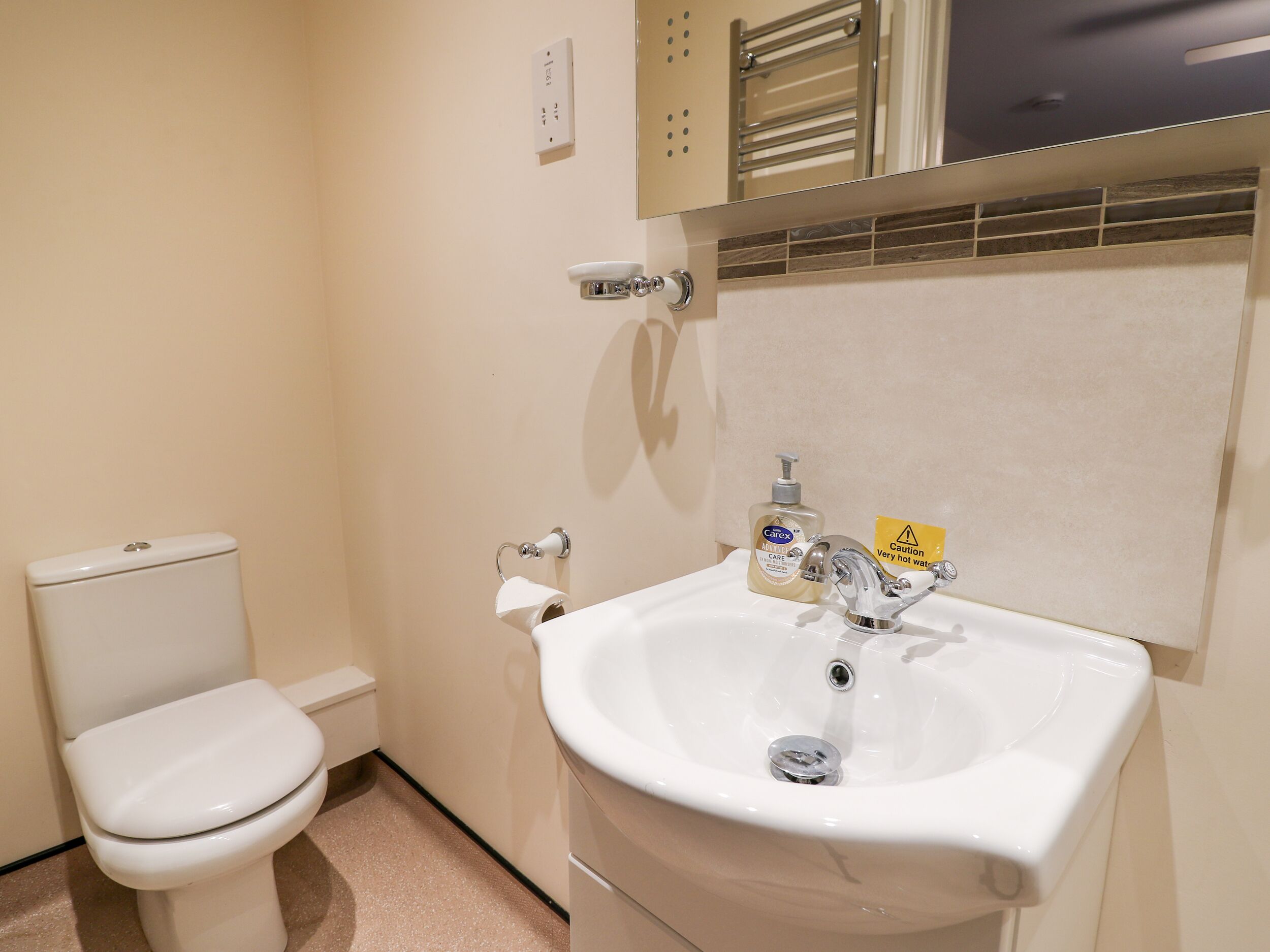 A bathroom with a toilet, sink, and a caution sign indicating hot water.