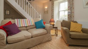 A living room with a beige sofa, a brown armchair, a patterned throw pillow, a lamp, and a staircase. - Drover's (Bridgwater)