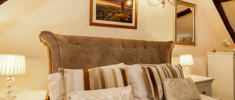 Un dormitorio con una cama grande, dos mesitas de noche, un candelabro, un cuadro enmarcado en la pared y un espejo sobre la cama.