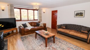 A living room with a brown leather sofa, a grey sofa, a wooden coffee table, and a TV on a wooden stand. - Green Hills Farm (Ulverston)