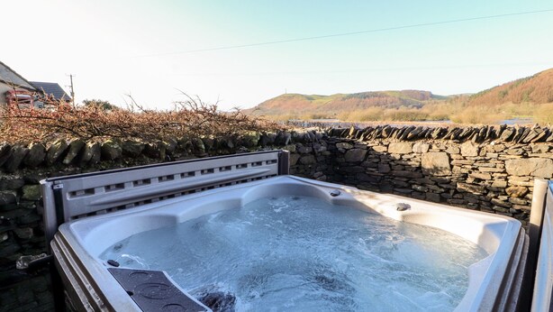 A hot tub with a stone wall and a view of hills. - Green Hills Farm (Ulverston)