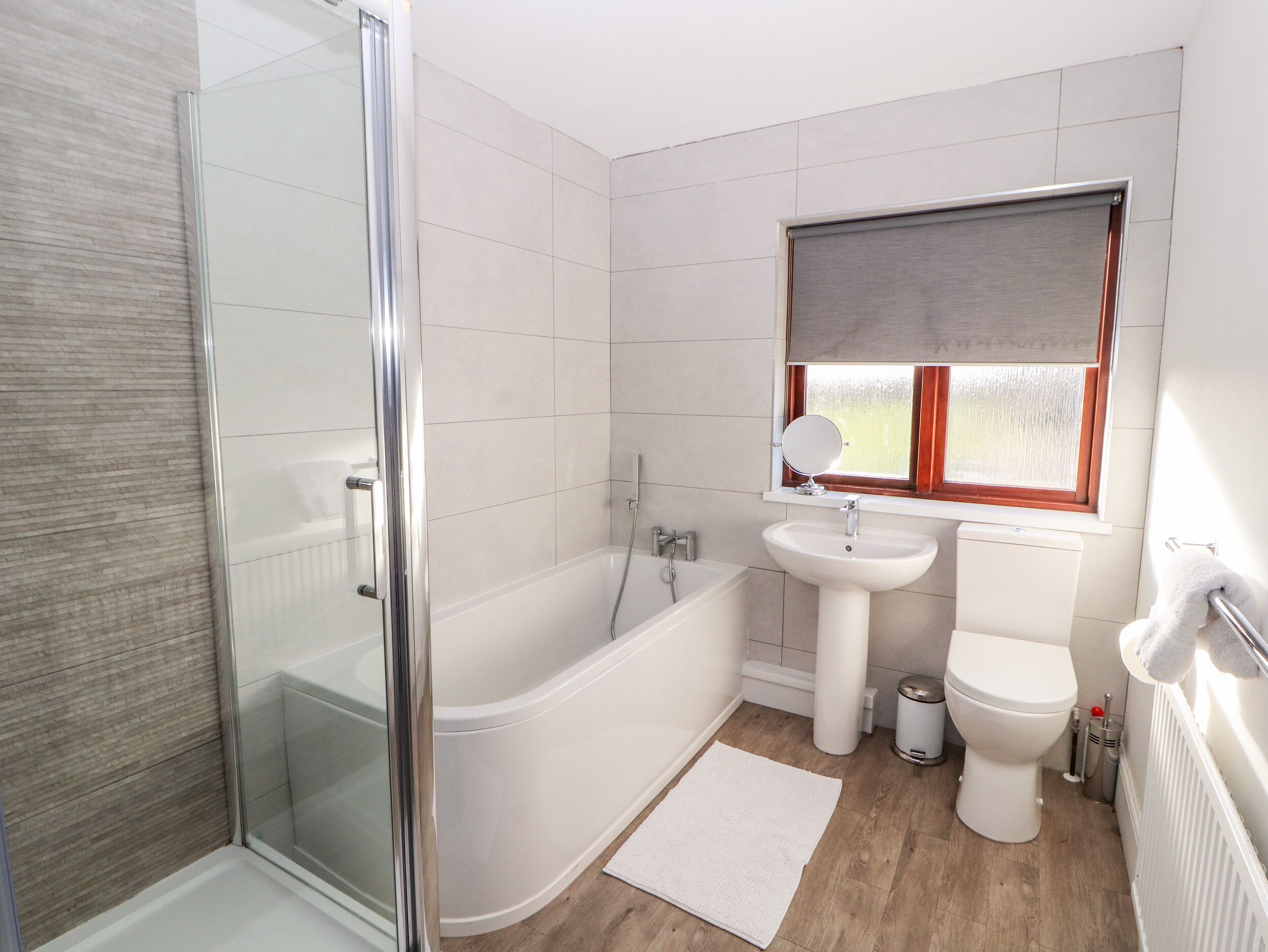 A bathroom with a glass-enclosed shower, a white bathtub, a sink, and a toilet.