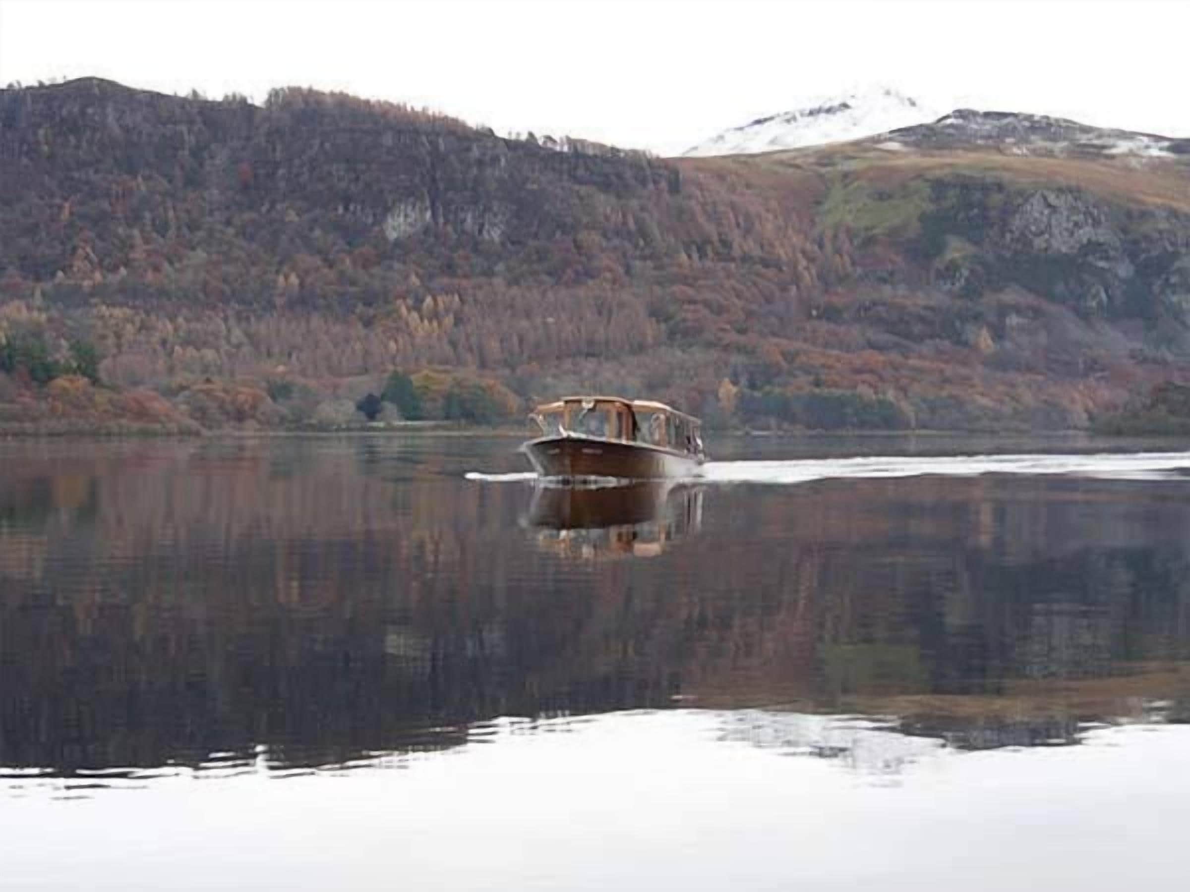 A boat on a calm lake with a forested mountain in the background.