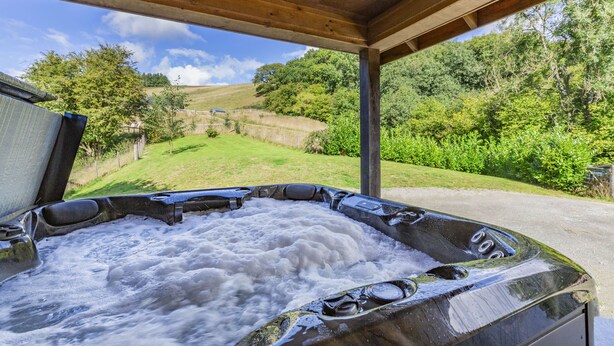 Een hottub met een houten dak en uitzicht op een groen landschap.