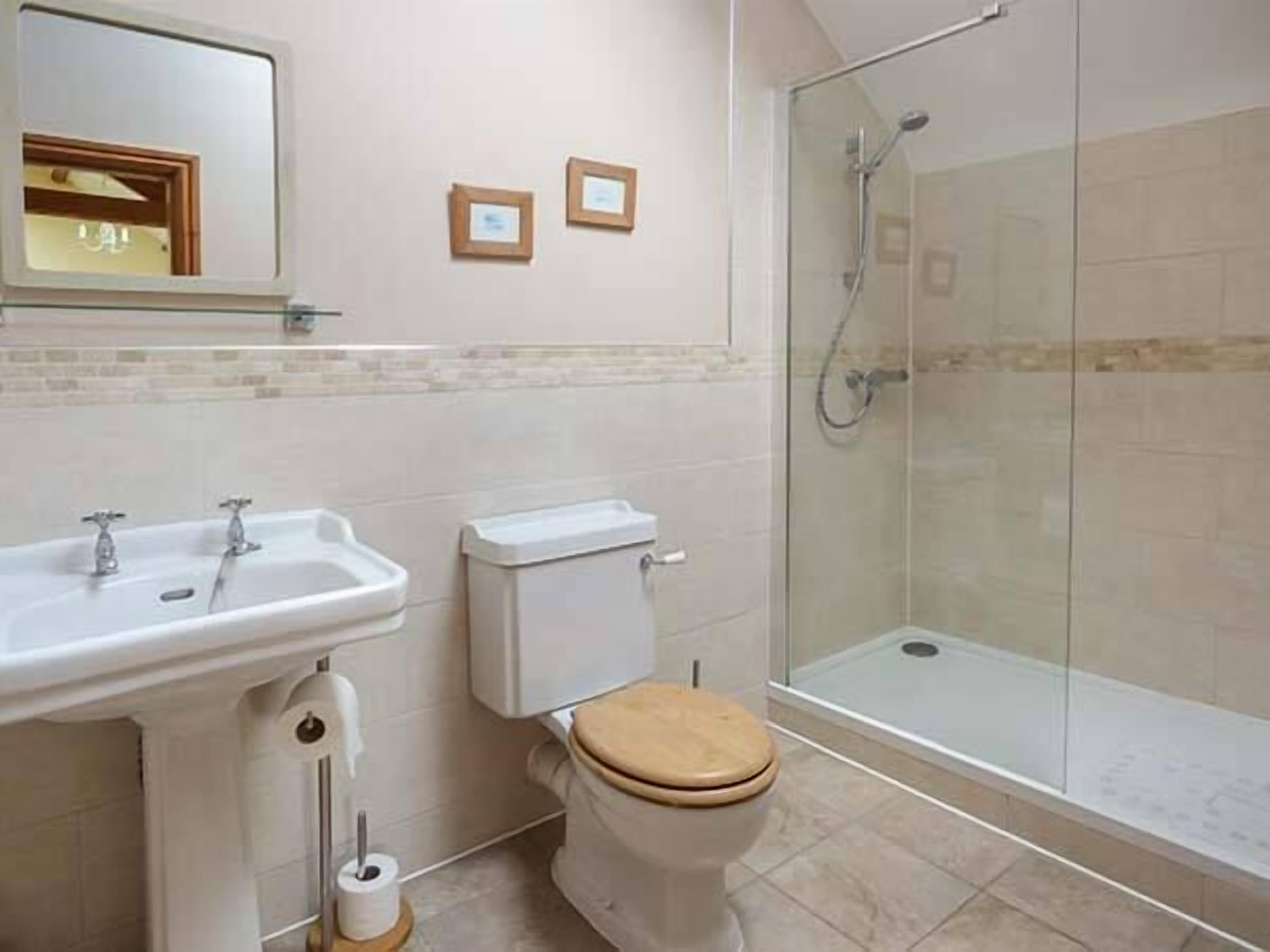 Une salle de bain avec une douche à parois de verre, des toilettes avec un abattant en bois et un lavabo avec un miroir au-dessus.