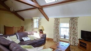 A spacious living room with a large leather sofa, a wooden coffee table, and a television on a wooden stand. - Bran Goesgoch (Holyhead)