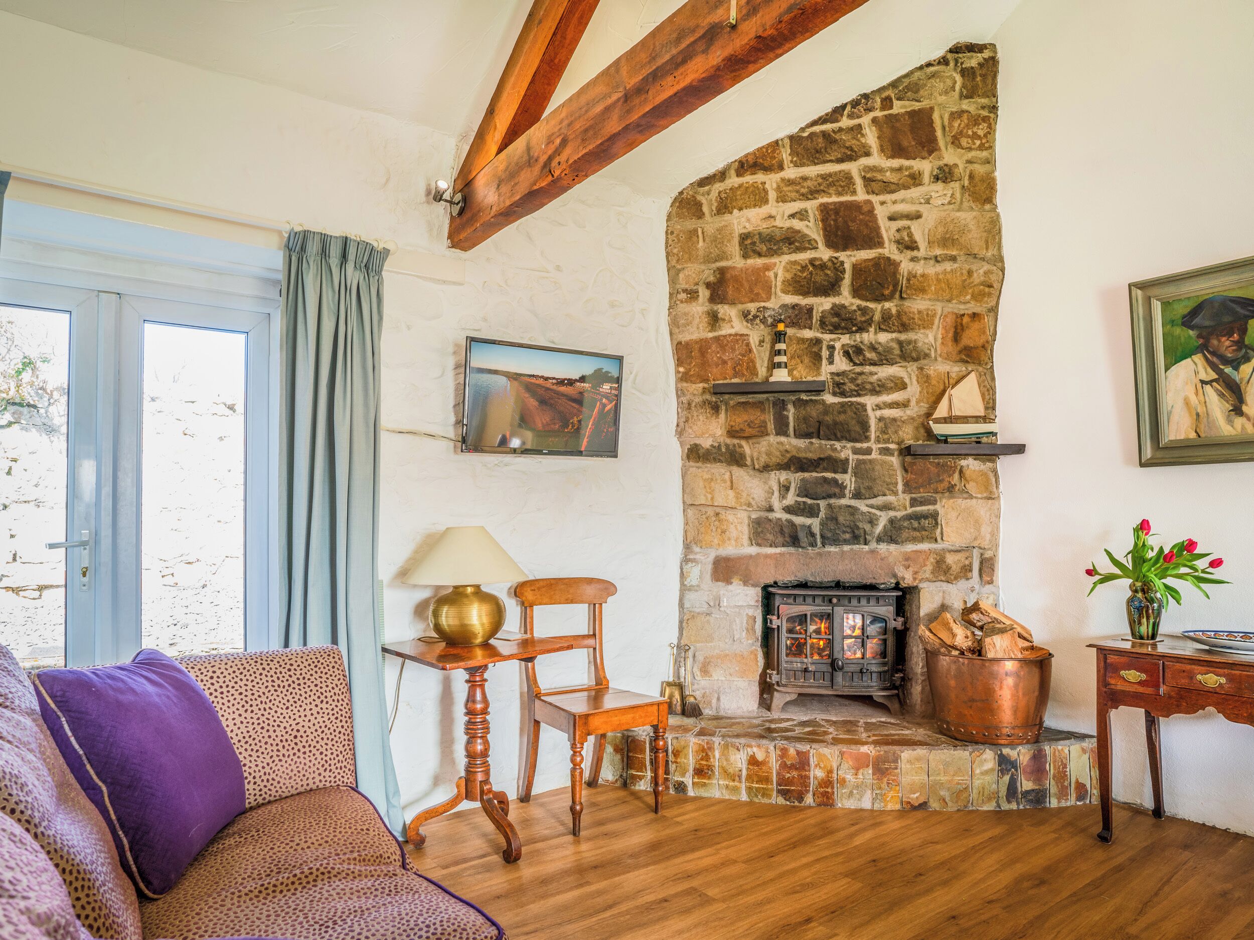 Ein gemütlicher Wohnraum mit Kamin aus Stein, Holzbalken, einer bequemen Couch und einem an der Wand montierten Fernseher.