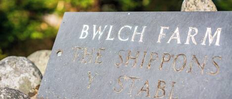 A sign with the text "BWLCH FARM THE SHIPPONS Y STABL" on a stone surface.