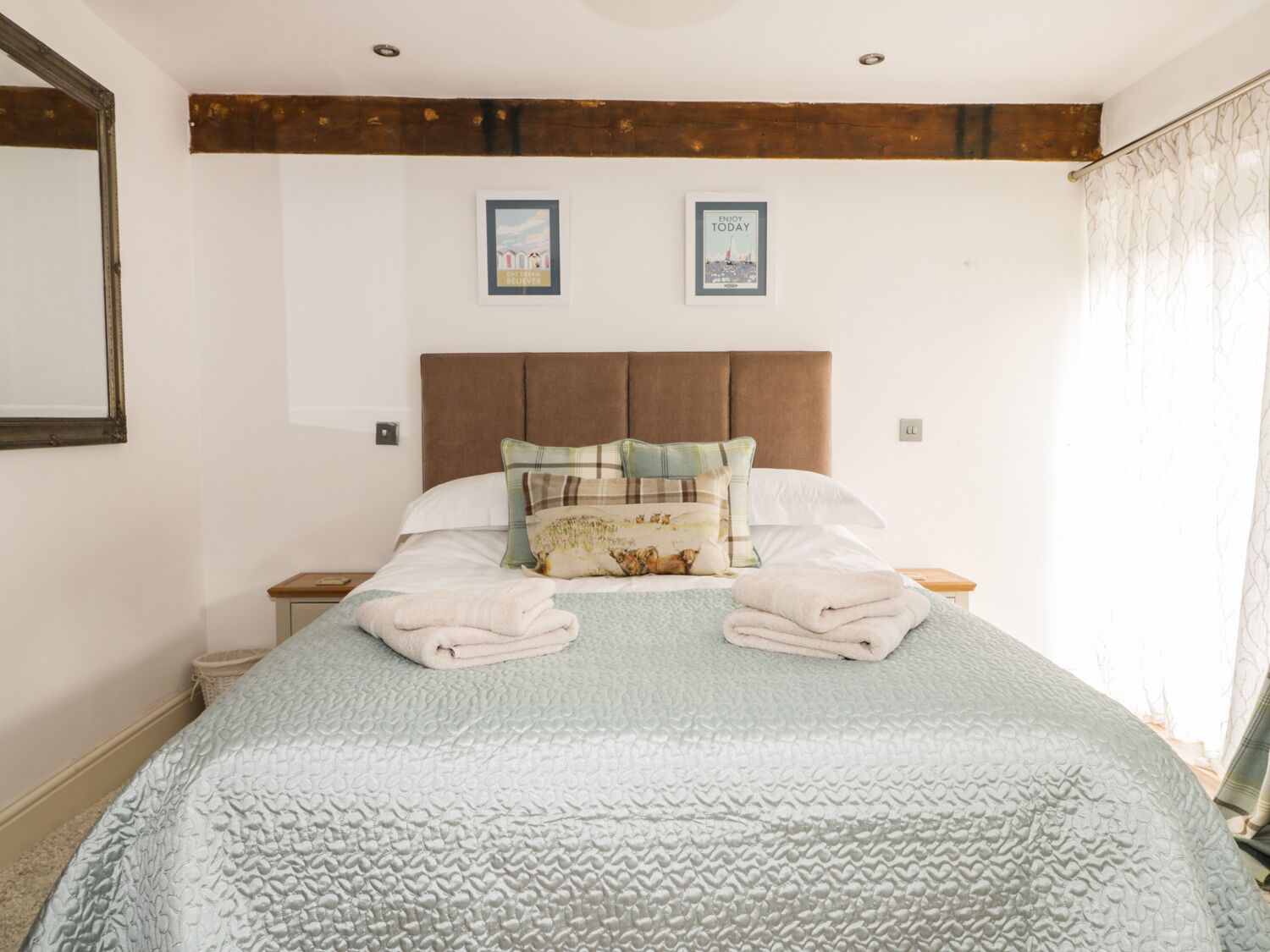 Un lit bien fait, recouvert d’une courtepointe matelassée, avec deux oreillers et des serviettes pliées. Deux tableaux encadrés sont accrochés au mur, au-dessus du lit.