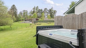 A hot tub with a wooden deck and steps, surrounded by a wooden fence and a grassy yard. - Maple - Woodland Cottages (Windermere)