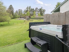 Un jacuzzi con cubierta de madera y escalones, rodeado por una valla de madera y un césped.